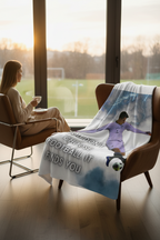 A candid, high-resolution photograph of a sophisticated living room. A thick, plush fleece blanket with the "You don't choose football, it finds you" quote subtly printed is draped elegantly over a leather armchair. A person in cashmere knitwear is sipping tea, looking out a large window at a rainy soccer pitch. Warm, golden hour lighting. Luxurious texture focus. 