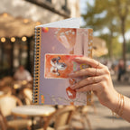 Social Media Image Prompt A high-quality influencer-style shot. A hand adorned with minimalist gold jewelry holds the closed notebook against a blurred, chic Parisian café background with outdoor seating. The Aries gold foil design is prominent. Natural sunlight. The aesthetic is sophisticated and aspirational.