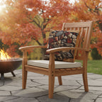 A photorealistic lifestyle photograph of the 'Autumn Stone Path Outdoor Pillow' placed on a high-end teak armchair on a flagstone patio. The background features mature maple trees with vibrant red and orange fall foliage, a fire pit with a gentle flame, and warm, golden hour sunlight filtering through. The pillow's texture is prominent and inviting. 