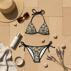 Social Media Prompt: A luxurious flat lay composition on warm, textured sandstone pavement. The Pebble Mosaic Bikini is laid out next to a wide-brim woven straw hat, oversized designer sunglasses, a bottle of high-end tanning oil, and a few smooth, natural pebbles. The lighting is natural, soft, and Mediterranean.
