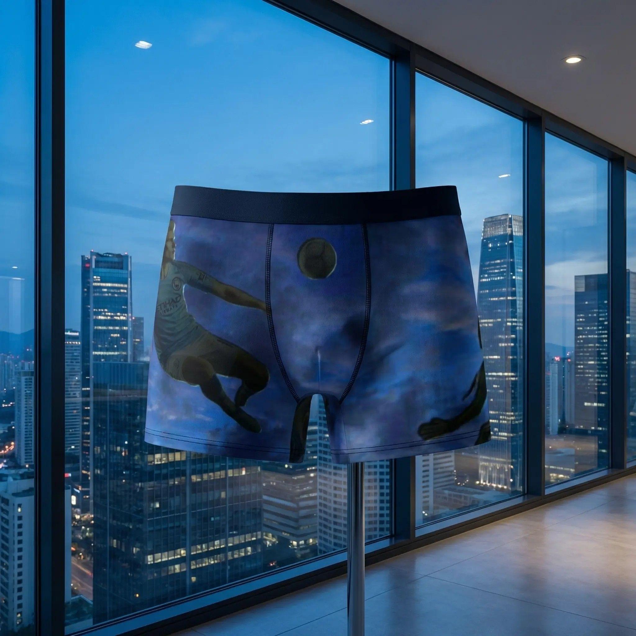 The boxer briefs placed against a large window overlooking a city at blue hour, the sky outside matching the deep blue tones of the product print, reflections on the glass, sophisticated vibe.